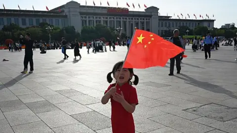 AFP via Getty Images A child plays holds the national flag in Tiananmen Square on China's National Day, which marks the 76th anniversary of the founding of the People's Republic of China, in Beijing on October 1, 2025. 