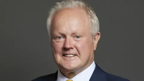 UK Parliament The Parliamentary portrait of Clive Jones, who has short, white hair.
