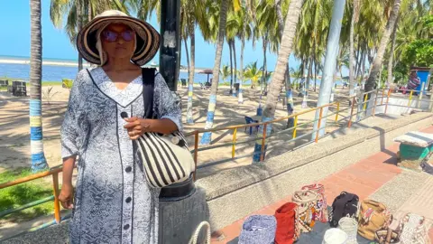 Sandra Aguilar stands above the mochilas she sells. She is wearing a patterned dress and holding a stripy mochila