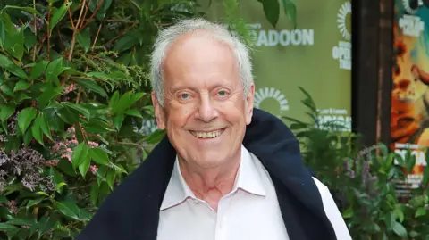 Getty Red carpet image of writer and broadcaster Gyles Brandreth wearing a white shirt and navy jumper