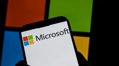 Getty Images A hand holding a phone with the red, green, blue and yellow square Microsoft logo.