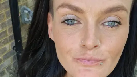 Handout Leanne purses her lips at the camera. She has light blue eyes and has two thin, silver nose rings - one in each nostril. She has a silver piercing outside her lower lip, and black hair.