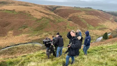 Bulldog Film Distribution A camera operator shoots down a hill on Exmoor, surrounded by various crew members, including the director in the foreground. They are surrounded by rolling hills.