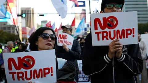 BBC A man and a woman hold up slogans that read 'No Trump'.