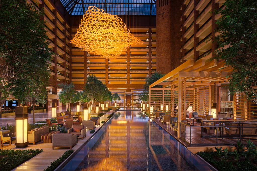 An atrium with reflecting pool running down the center, and various seating areas on either side, surrounded by the hotel.