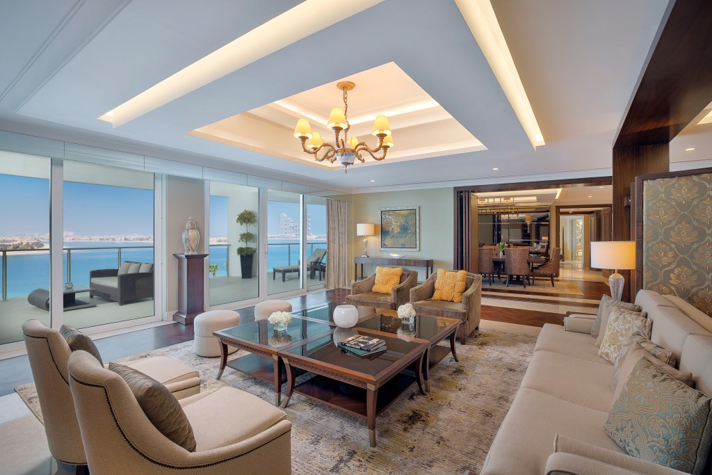 The living area of the suite, with couch and chairs looking out at the balcony and the view, with a separate dining room in the background.