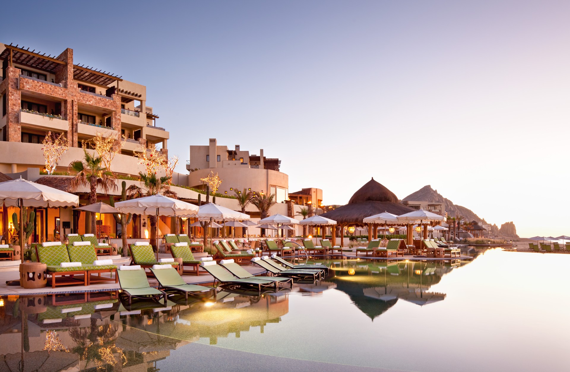 The pool of the hotel, with lounge chairs and umbrellas, with the hotel in the background