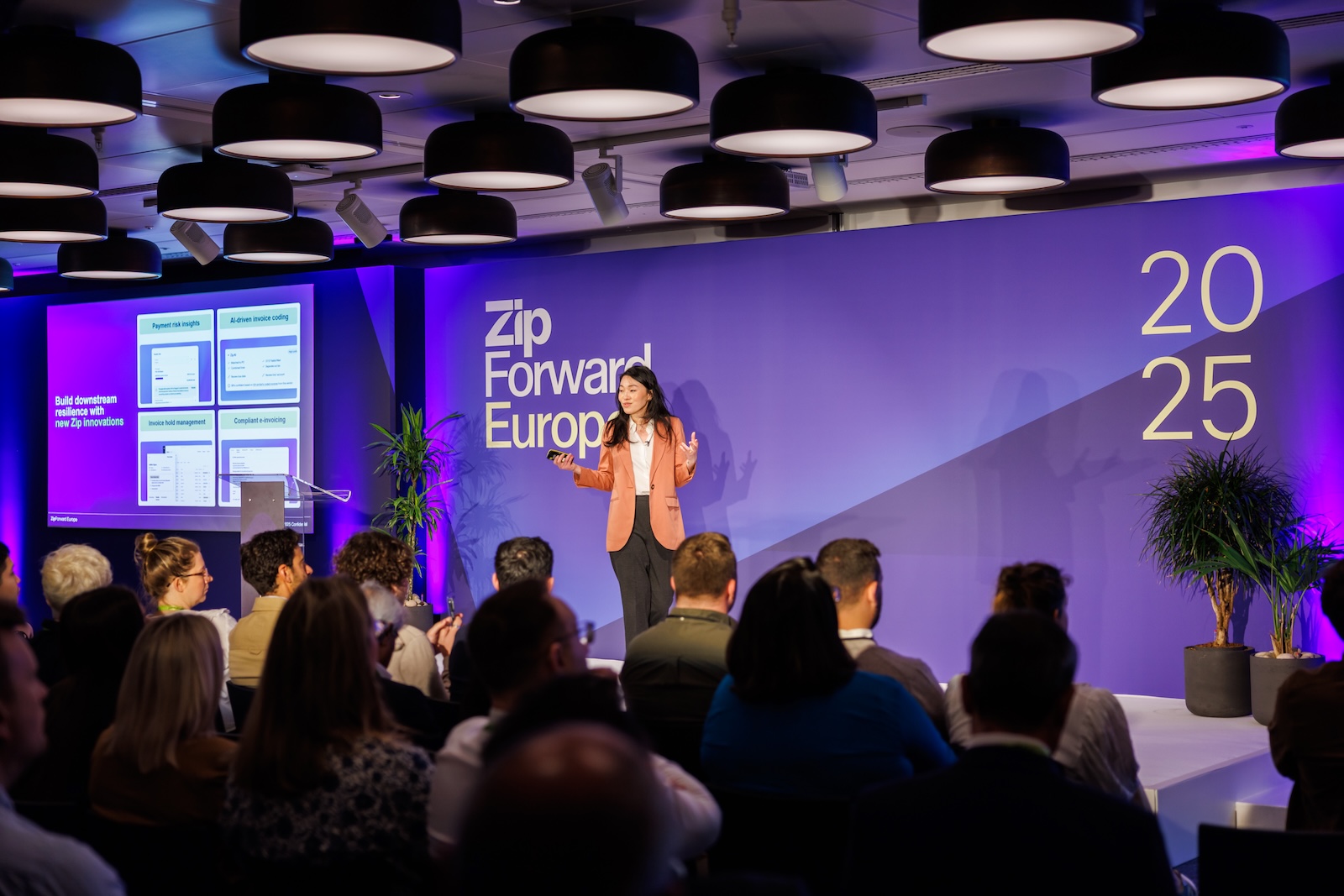 Speaker on stage with purple sign, digital screen, and dramatic lighting at Convene 22 Bishospgate