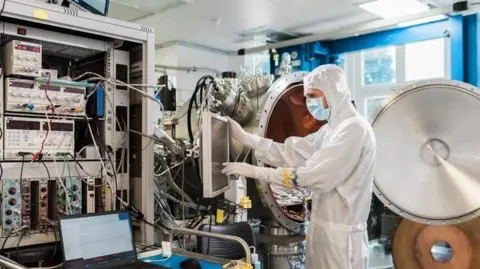 Mullard Space Science Laboratory A scientist wearing a white hazmat suit and a blue face mask, works on a very high tech piece of engineering at the Mullard Space Science Laboratory.