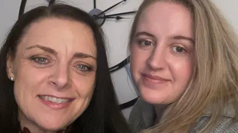 Family handout Abbigail Smith and her mum, who has long brown hair and is smiling with a wall clock behind them both. Abbi is wearing a grey jumper and smiling.