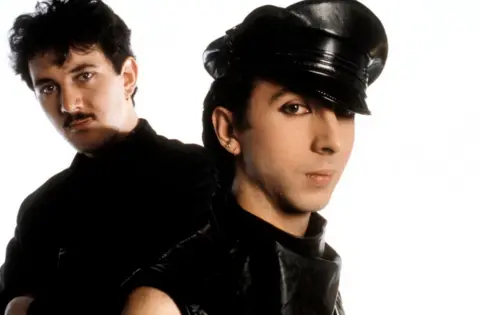 Getty Images Soft Cell (Dave Ball and Marc Almond), both wearing black, Marc Almond has a cap on.