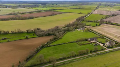 PA Wire Aerial view of green fields lined by trees and paths. A couple of houses can be spotted among the fields.