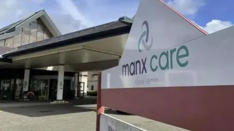 BBC A large white Manx Care sign outside the entrance to Noble's Hospital. It has lettering in grey and green in both English and Manx.