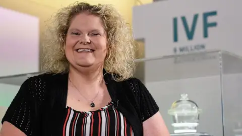 Leon Neal/Getty Images Louise Brown smiling into the camera. She is stood in front of a banner that reads 'IVF'.