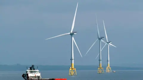 Getty Images A wind farm off the coast of Aberdeen Three wind turbines on the water spin, while a small ferry sails past nearby