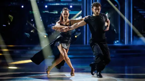 PA Media Alexis Warr and George Clarke dancing the Paso Doble on Strictly. The lights are dimmed, with spotlights reflecting on the floor.