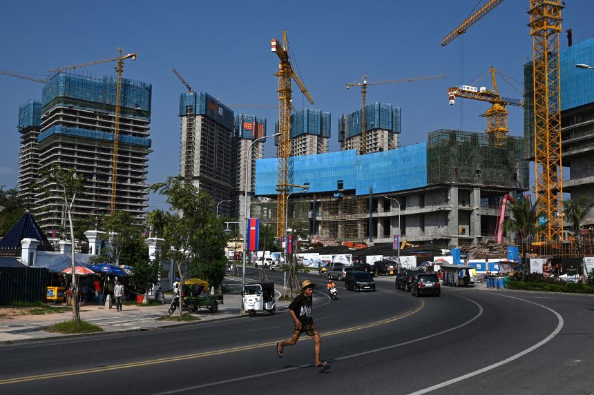 This photo taken on April 8, 2025 shows a youth running across a street past the site of the under-construction luxury seafront shopping resort 'Peninsula Bay' in Sihanoukville.
