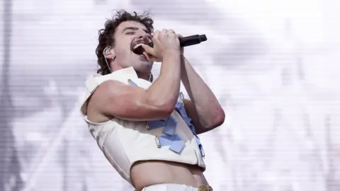 EPA-EFE/REX/Shutterstock Benson Boone performs on stage. He is holding a microphone in both hands.