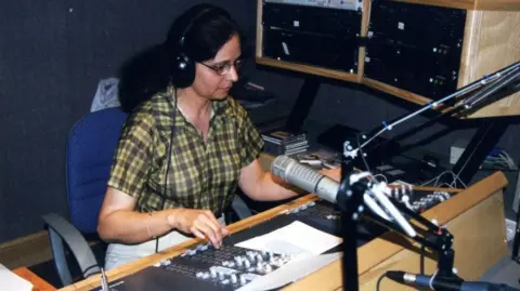 Stories That Made Us archive A woman wearing headphones sits in front of a microphone at a radio desk in the 1990s.