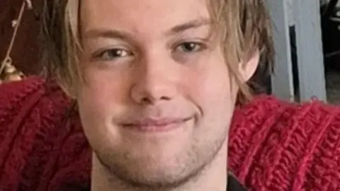 West Yorkshire Police Ashton Kitchen-White smiling at the camera with a stubble beard and brown 