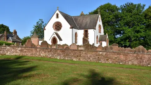 Mitchell family A whitewashed church with sandstone features around the windows, sitting on a hill surrounded by gravestones and a boundary wall