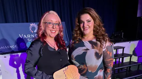 Supplied Jolie Bartley, Head of Performing Arts at Varndean School, pictured with West End star Jodie Prenger. The pair are pictured at Varndean School and Jolie is holding her award. Jolie is wearing a black top and has blonde/red dyed hair. Jodie is wearing a flowered dress and has long brown hair.