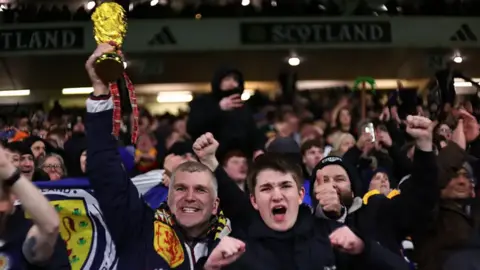 Getty Images A Scotland fan celebrating while holding the World Cup aloft.