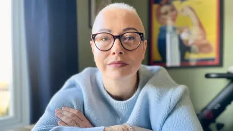 Mark Norman/BBC Close up of Jules Fielder wearing glasses and a blue jumper looking to camera