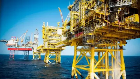 Getty Images Image of an oil rig in the North Sea - yellow stanchions reach down in the water from several platforms, against a blue sky and deeper blue sea