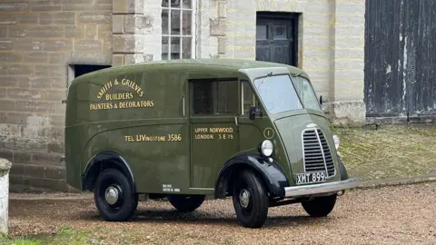Morris Commercial An olive green-coloured original Morris JE van is parked up on gravel in front of a stone building. It has 'Smith & Grieves Builders Painters & Decorators' painted on the side, along with 'Tel: Livingstone 3586' and 'Upper Norwood. London. S E 19'.  