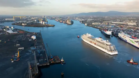 Belfast Harbour A shot from above of Belfast Harbour. There is water in the middle and land on either side. Two yellow cranes are visible in the distance. There is a cruise ship in the middle of the harbour and a Stena Line ferry on the right. There are also smaller boats.