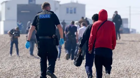 PA Media A police officer escorts a group of people thought to be migrants ashore from the Dungeness lifeboat in Dungeness, Kent, after being picked-up following a small boat incident in the Channel