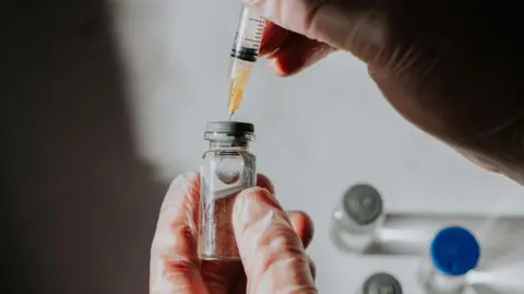 Getty Images A scientist draws liquid medicine through a syringe from a vial