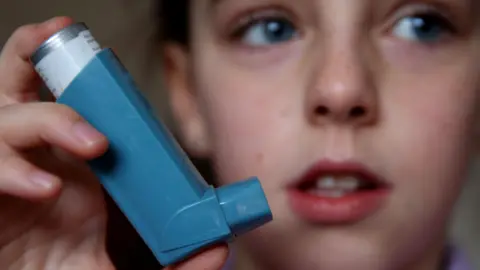 Peter Byrne/PA Wire Close-up image of a blue inhaler device in a child's hand