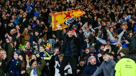 SNS Dozens of Scotland fans celebrating at the final whistle at Hampden. They have scarves and banners.