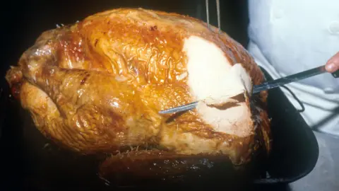 BBC A turkey being carved with a slim metal knife and a pronged fork by a person in a white coat.