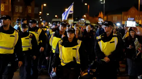 PA Media A group of officers are walking down a street outside Villa Park, most are male but in the middle is a white female officer wearing a black cap, all of them are wearing hi-vis vests
