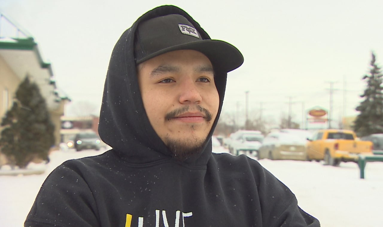 Man wears a black hooded sweatshirt and stands outside in a snowy parking lot