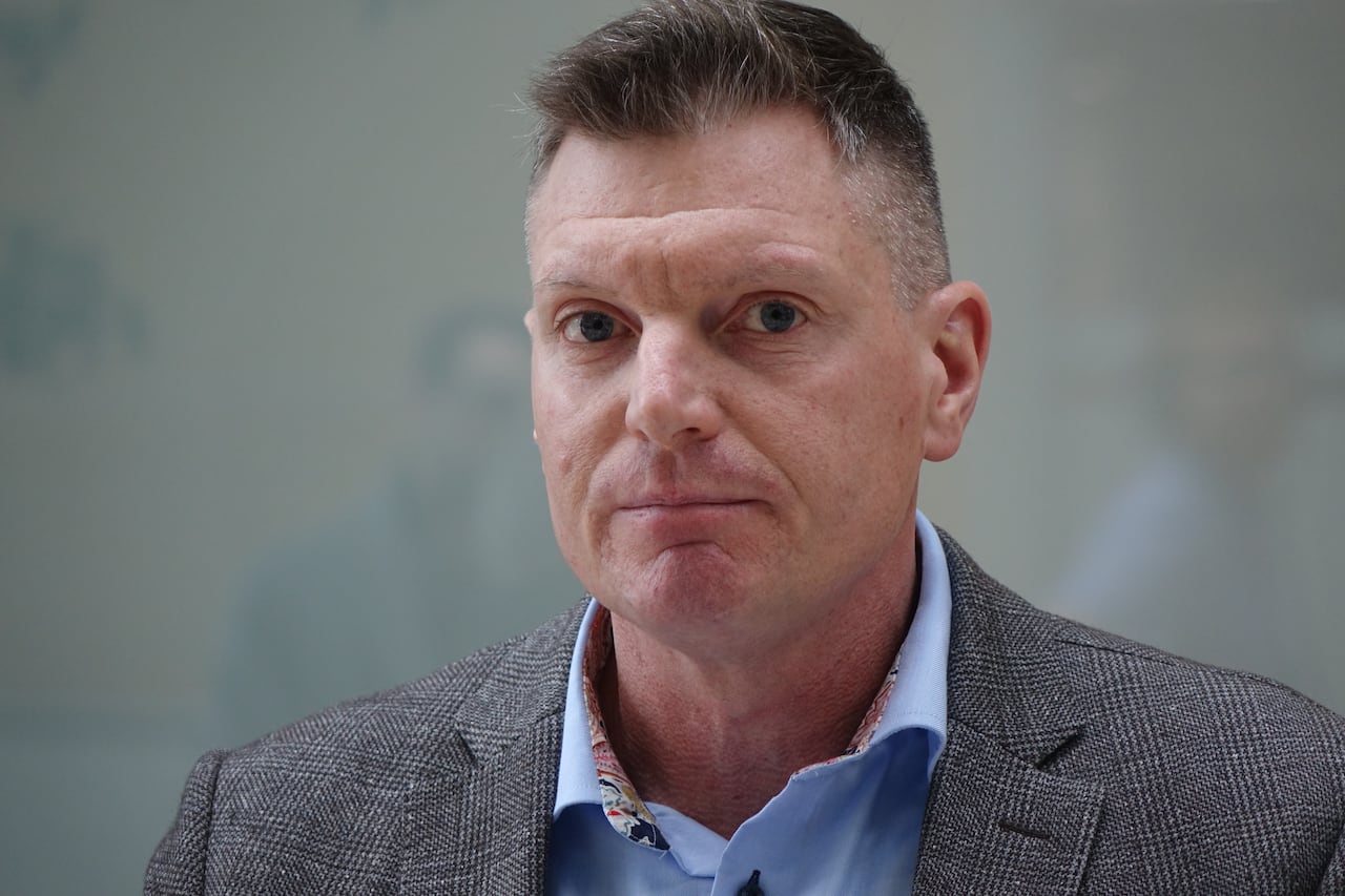A man wearing a grey suit standing in a lobby.