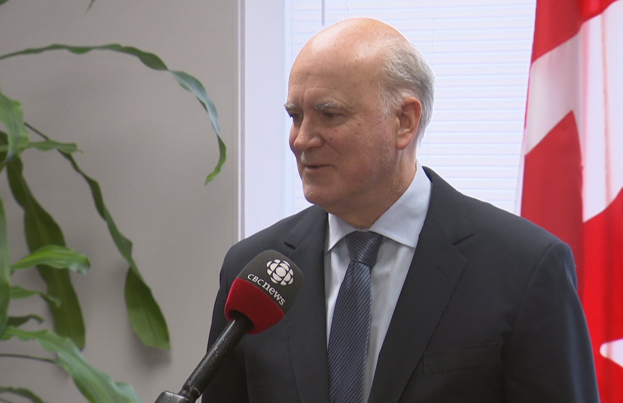 A close-up shot of a man wearing a dark suit and tie, speaking into a CBC News microphone.