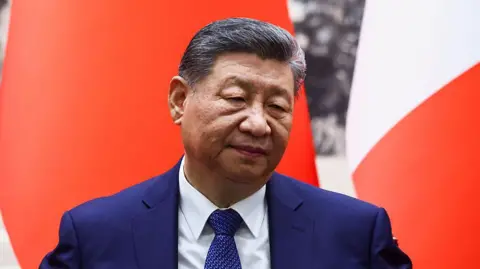 Getty Images Chinese President Xi Jinping attends a signing ceremony for agreements at the Great Hall of the People in Beijing on December 4, 2025. He is wearing a dark blue sit and in front of a red and white background.
