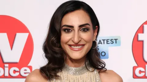 Getty Images Punam Krishan smiling in a smart jewelled cream dress posing in front of a TV Choice-branded backdrop at the TV Choice Awards 2025