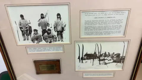 Adam Partridge Auctioneers The presentation case has two black and white group photos of the expedition member wearing cold weather gear and hats as they stand in the snow holding ski poles. There is a brass plaque and three boxes of typewritten information which is to small to read in this photo.