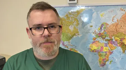 Mike Smith standing in front of a map of the world with pins in it to show where donations have been transported to from the Nottingham centre. 