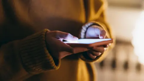 Getty Images A person in a yellow jumper uses a smartphone.