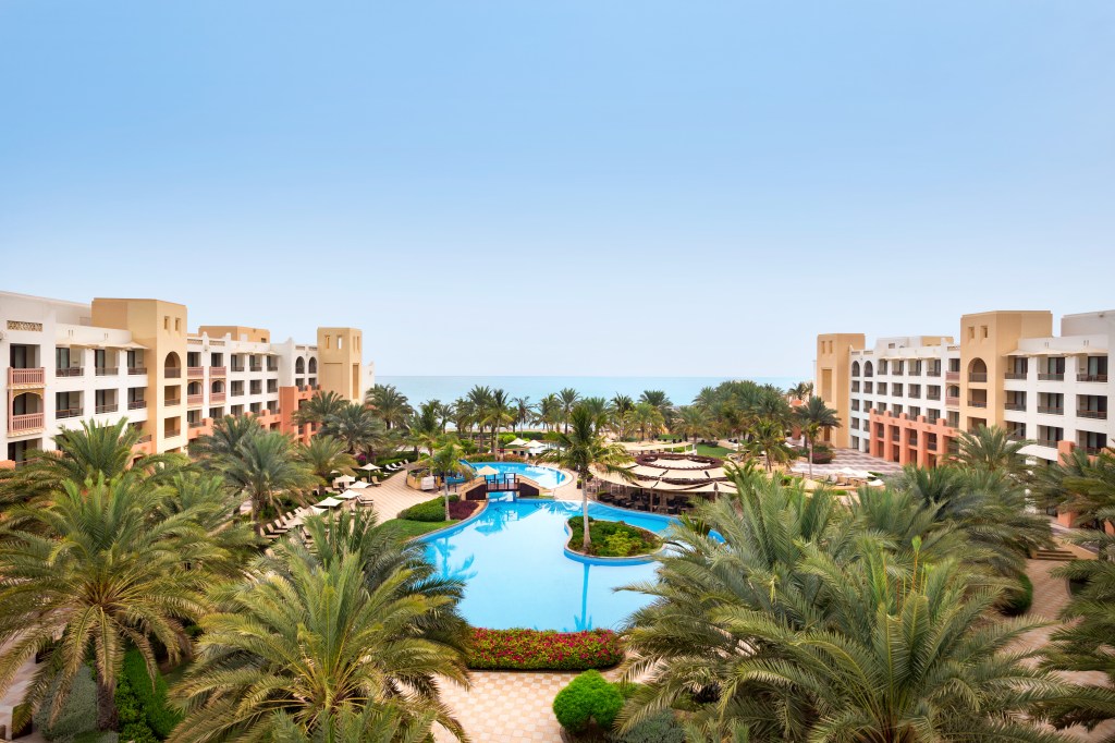The pool in the middle of the hotel, surrounded by palm trees, with the ocean in the distance.
