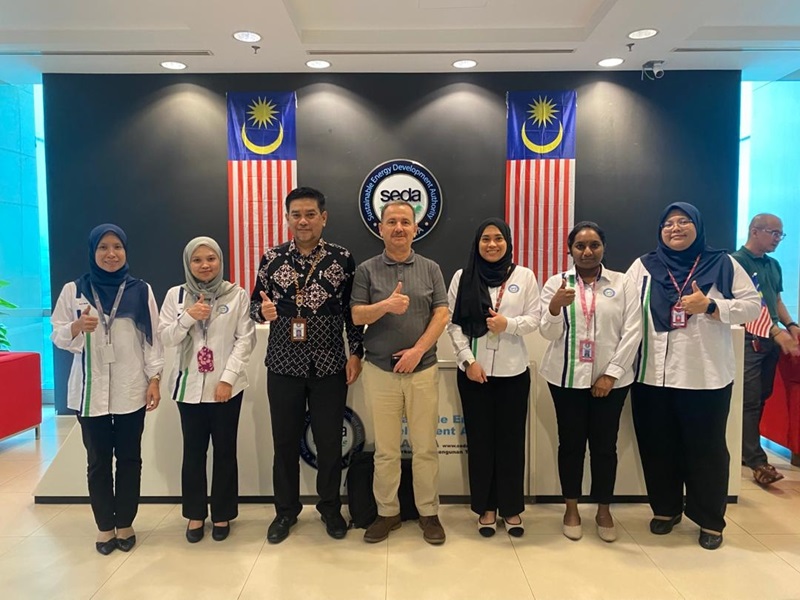 Seven people smiling at camera with backdrop of Malaysian flags