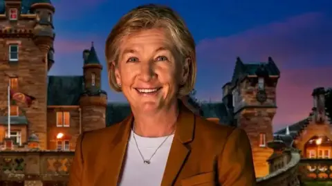 BBC/Studio Lambert/Cody Burridge/Matt Burlem The Traitors contestant Amanda Collier wearing a brown blazer and white top. She is stood in front of a castle at sunset.